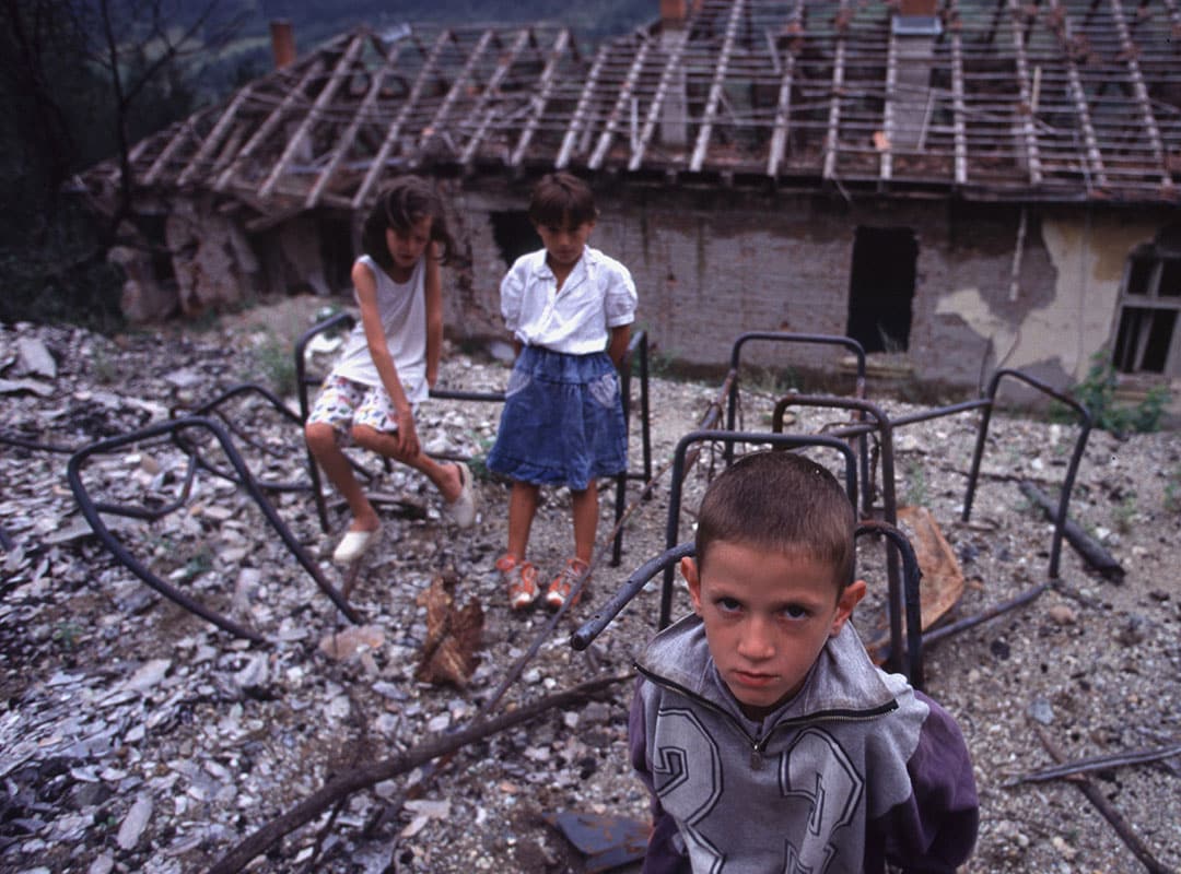 Barn som står foran en nedbrent skole.
