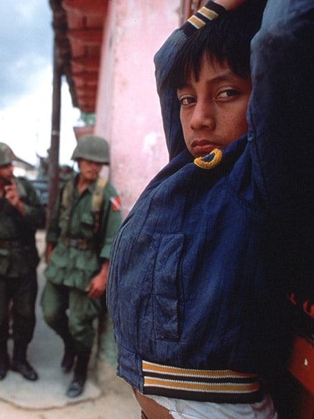 Et barn lener seg mot en vegg foran to soldater.