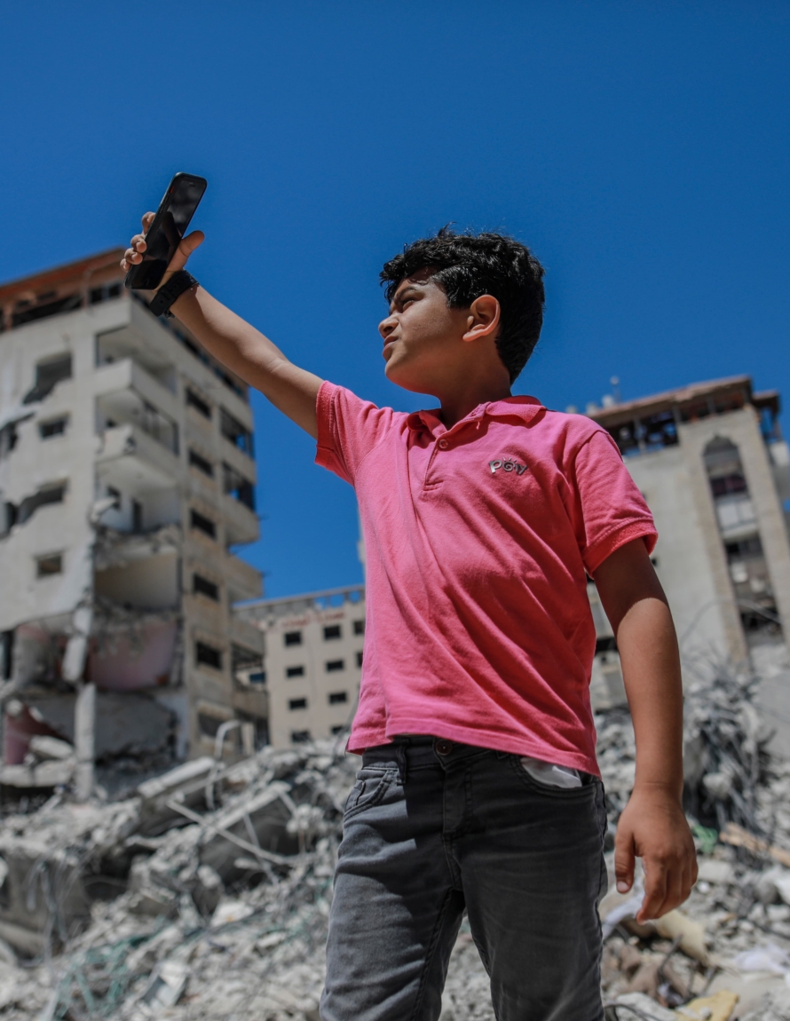 Ung gutt tar selfie på Gaza foran ødelagte bygninger