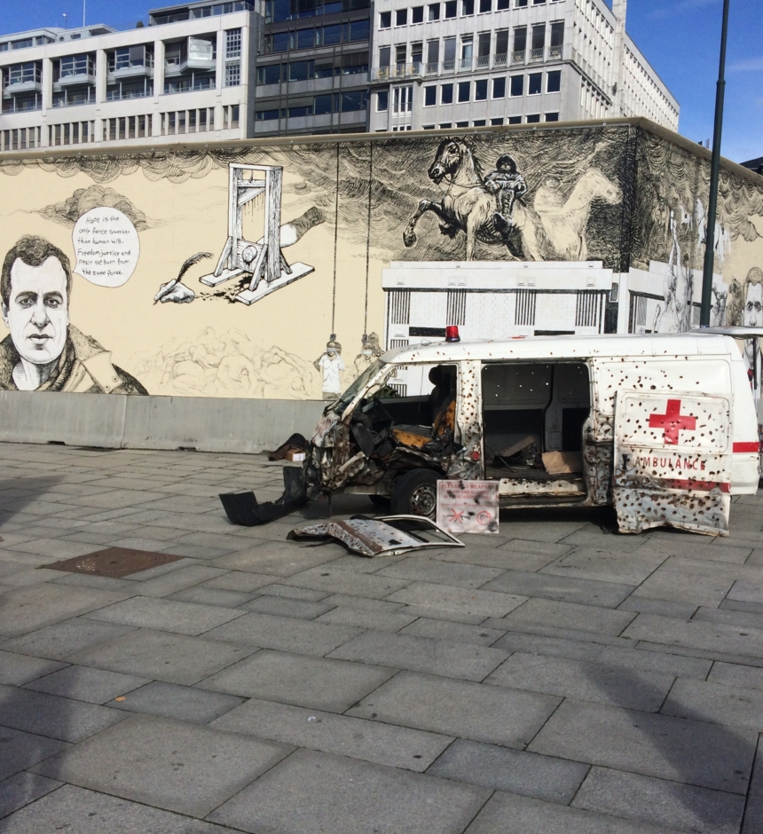 Utbombet Røde Kors ambulanse foran en grafittimalt mur med politiske budskap