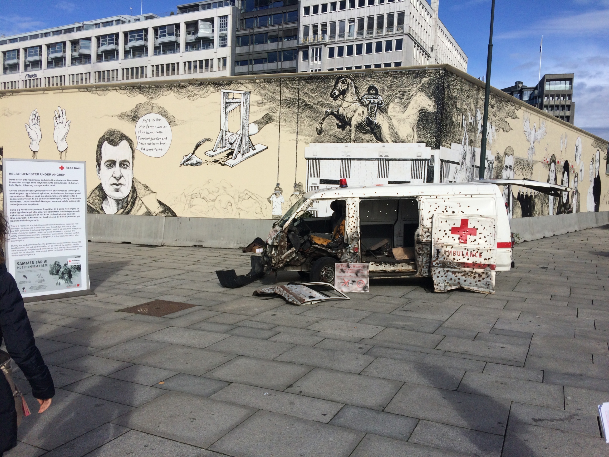 Utbombet Røde Kors ambulanse foran en grafittimalt mur med politiske budskap