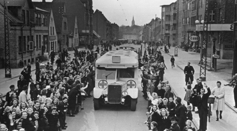 En hvote bussen med røde kors kjører gjennom en jublende folkemengde