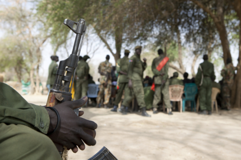 I forgrunnen en soldat som sitter med et gevær i hånden. Uskarpt i bakgrunnen sees en gruppe soldater.