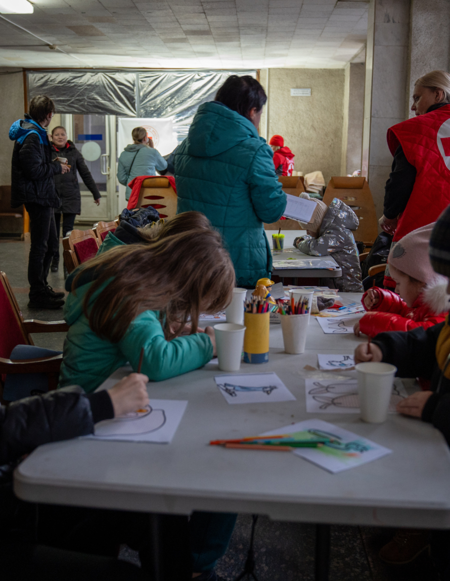 Barn sitter og tegner ved et ankomstsenter satt opp av Røde Kors