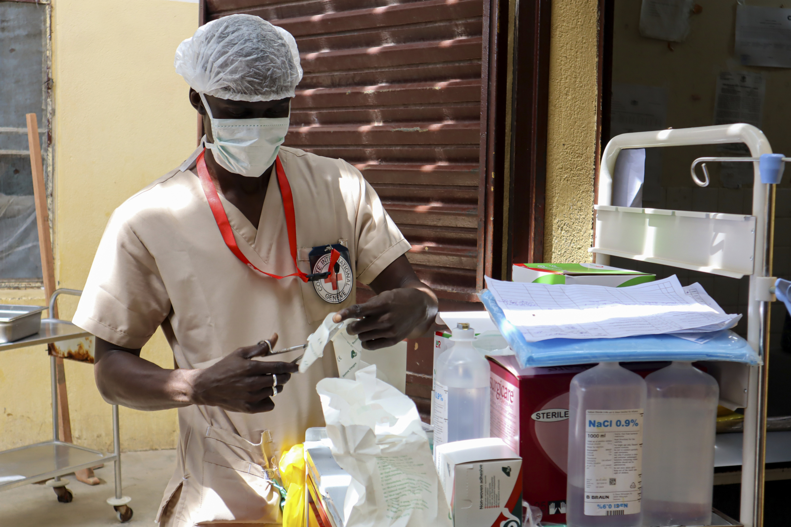 Nærbilde av en lege med hårnett og munnbind som klargjør medisinsk utstyr fra en utstyrstralle.