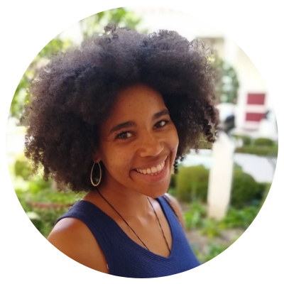 Portrettbilde. En ung kvinne med stort, mørkt hår iført en blå singlet kikker smilende inn i kameraet.