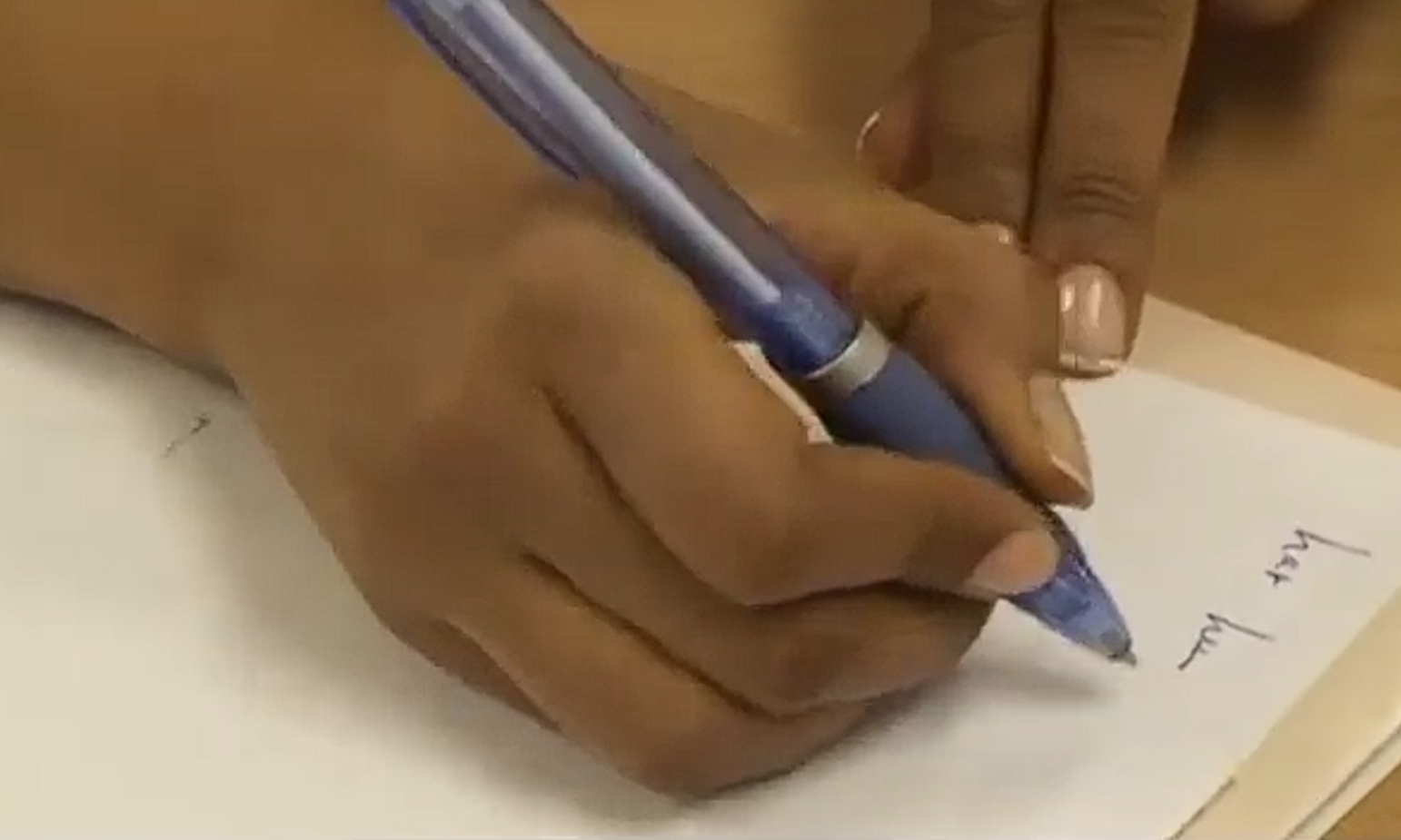 Bildet viser en hånd som skriver med penn på et papir.