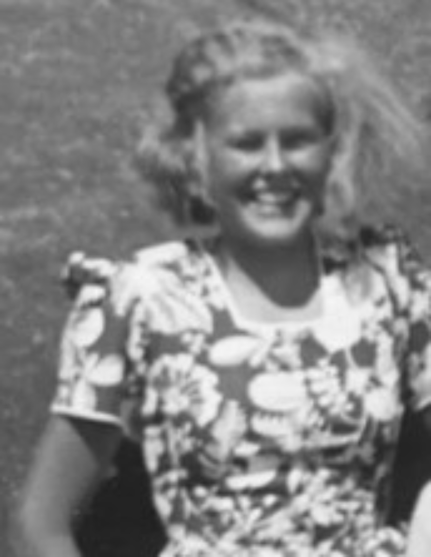 Et gammeldags sort-hvitt foto av en jente med blondt hår som smiler til kamera. Hun har på seg en blomstrete kjole.