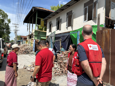Jørgen Haldorson fra Norges Røde Kors ser på hvordan hjelpearbeidere fra Myanmar Røde Kors distribuerer nødhjelp. I bakgrunnen flere delvis sammenraste bygninger.