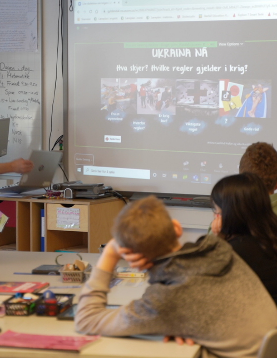Bilde sett fra bakersti i et klasserom. Vi ser elever som sitter og ser på Live skoletime på en storskjerm.